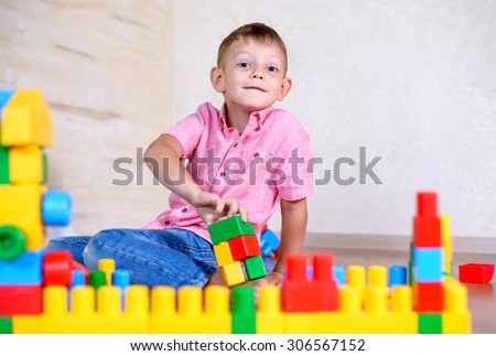 Cute cheeky young boy playing at home with colorful plastic building blocks holding up a toy to the camera with a grin