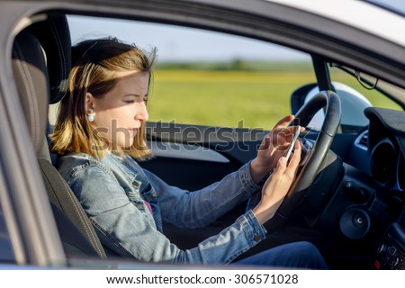 Dangerous female driver reading a text message on her smartphone and taking her attention off the road, profile view
