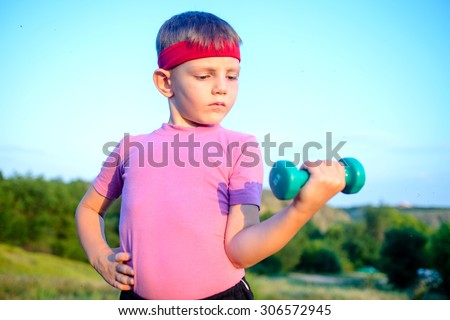Close up Strong Cute Boy with Red Headband Doing an Outdoor Exercise and Lifting Small Dumbbell Against Blurry Nature Background.