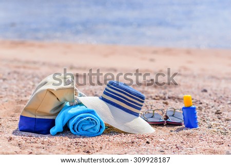 Beach Bag and Supplies for Day at the Beach on Sandy Shore - Sun Hat, Flip Flops, Towel, Sunscreen Lotion, and Beach Bag on Sunny Beach