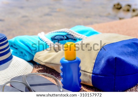 Beach gear arranged neatly at the waters edge on a sandy tropical beach with a sunhat, bag, slip slops, towel, sunglasses and suntan lotion conceptual of a summer vacation