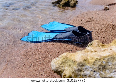 Pair of blue rubber fins or flippers on the seashore lying alongside a rock at the edge of the ocean ready to go swimming or skin diving