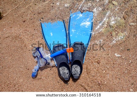 Skin diving equipment standing ready on a beach on the sand at the edge of the sea with a pair of flippers, snorkel and goggles, conceptual of recreational activities on summer vacation