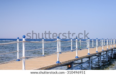 Wooden pier with safety ropes at a tropical resort leading across the shallow tidal water to wooden buildings at the end in deep water