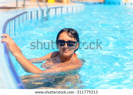 Smiling attractive woman in sunglasses floating in a swimming pool looking up camera
