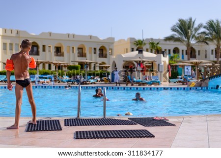Sharm El Sheikh,Egypt,28 July 2015:Young boy wearing red plastic arm bands or water wings standing with his back to the camera looking out over a resort swimming pool enjoying his summer vacation