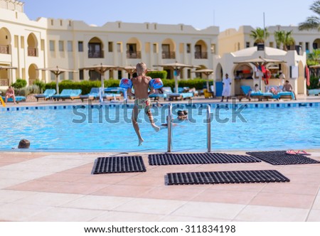 Sharm El Sheikh,Egypt,28 July 2015:Boy jumping into a swimming pool at a tropical resort or hotel viewed from the rear with the hotel buildings in the background