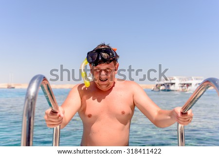 Smiling man preparing to go snorkeling standing holding onto the rails on a dive boat with the ocean behind