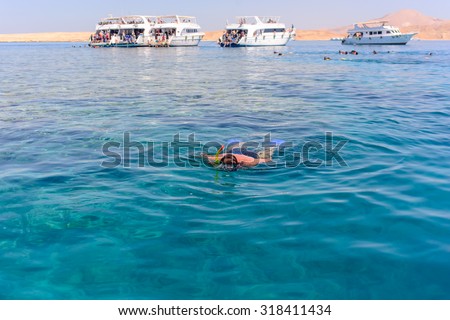 Man enjoying his summer vacation in the tropics skin diving off a tour boat floating face down in the water viewing the marine creatures below with additional tour boats visible in the background