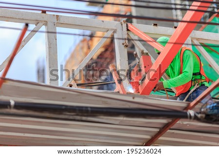 people work welding steel bars on construction site. He stand on the scaffold wear green T-shirt ,cable front of picture and building background