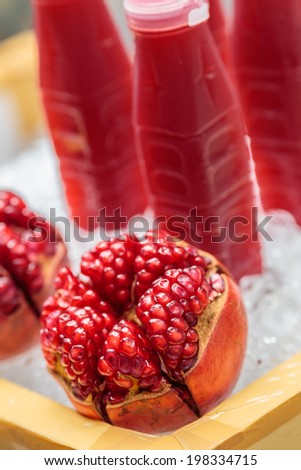 Ripe pomegranates with juice and ice on box ,fresh red pomegranates ,yellow box ,plastic bottle of juice