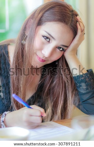 Asia Woman writing data document Thinking smile look at camera in the Office ,hold the head with hand