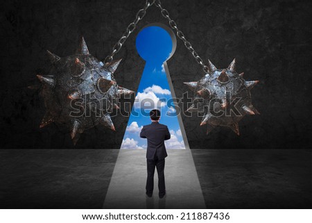 difficult path of businessman front of spike wrecking ball and chain against keyhole on old grunge black wall and bright blue sky background in concept of obstacle and trap on the way of a business