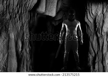 A dangerous man wearing a balaclava camouflage and holding knife standing in the dark cave