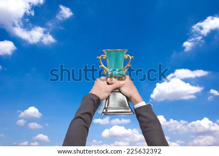 Business hand holding a champion trophy against blue sky