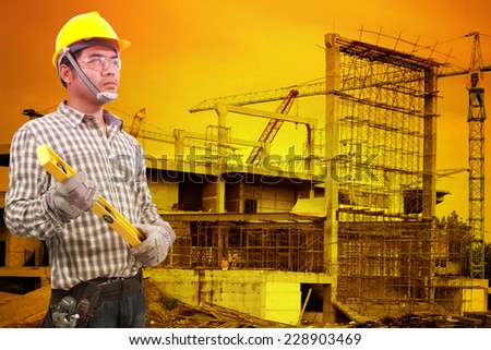 technician in protective safety equipment goggles hard hat and water level against building construction crane with beautiful sunset