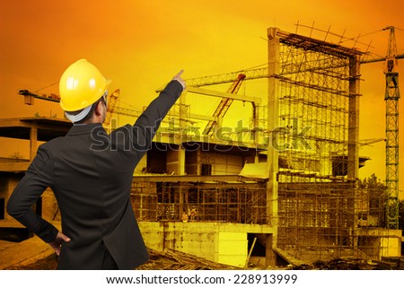 rear view of engineer pointing to the future building construction crane with beautiful sunset
