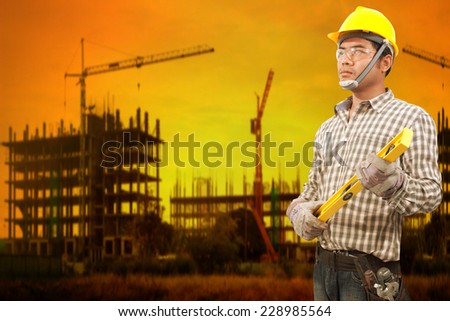 technician builder in protective safety equipment goggles hard hat and water level working at high building construction site against beautiful sunset