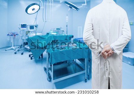 rear view image of doctors with stethoscope in a hospital pose arms crossed behind back looking at operating room of a modern hospital