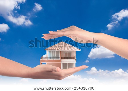 house in hands representing home ownership and the real estate business against blue sky