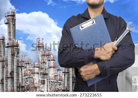 mechanic holding a clipboard of service order with wrench for working at petrochemical oil refinery in blue sky