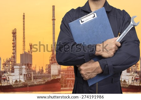 mechanic holding a clipboard of service order with wrench for working at petrochemical oil refinery in sunrise