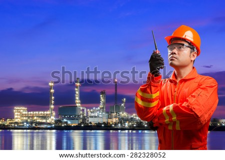 Engineer with radio communication in action for working at oil refinery petrochemical industrial plant at twilight