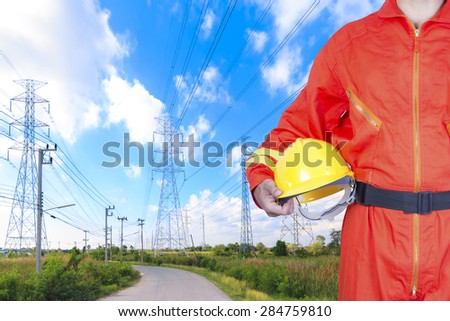 Engineer holding hard hat for working at high voltage power pylon against blue sky