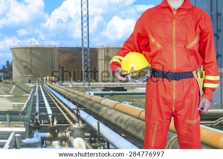 Technician holding hard hat for working at pipe line connection to oil tanks in petrochemical oil refinery