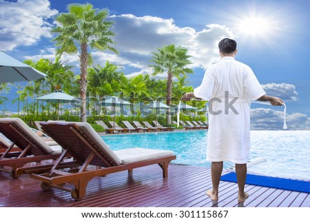 man in bathrobe on edge of swimming pool and relaxing
