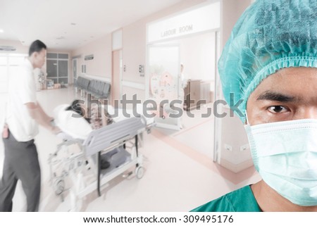 Mature male surgeon looking at camera and medical active staff pushing stretcher gurney bed in labour room of hospital corridor with female patient pregnant in emergency status