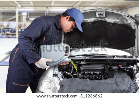 Car mechanic replacing and pouring oil into engine at maintenance repair service station