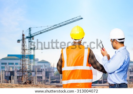 Engineer and foreman looking at blueprints use radio communication for command working against building construction crane