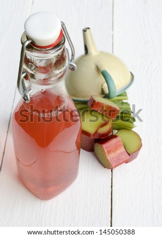 A bottle of rhubarb juice and pieces of rhubarb and a funnel
