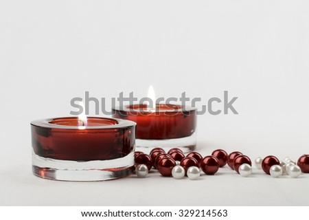 Two rich red glass candle holder votive and red white pearls. White background, horizontal, copy space.