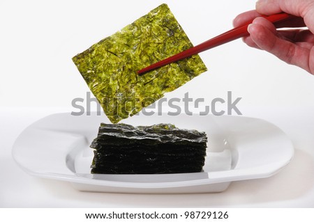 Roasted Seaweed, held with red chopsticks.  Isolated on white