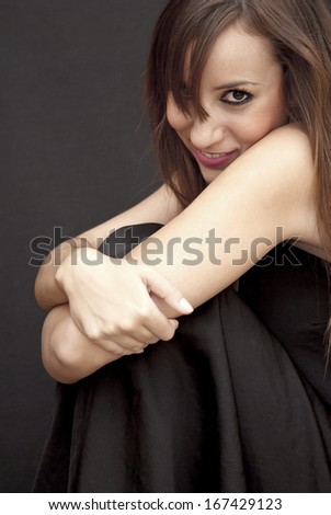 Beautiful Brunette Girl hugging her knees over black background