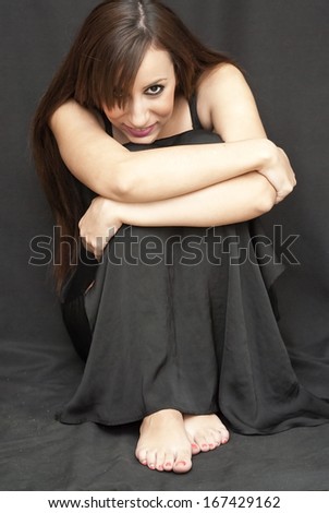 Beautiful Brunette Girl hugging her knees barefoot over black background