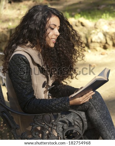 Beautiful woman on a park bench reading a book in autumn
