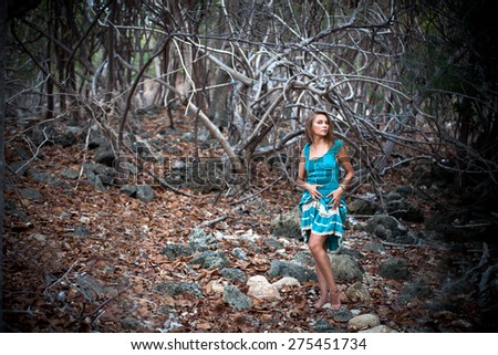 Portrait of a beautiful young woman in turquoise dress standing by trees In jungle forest