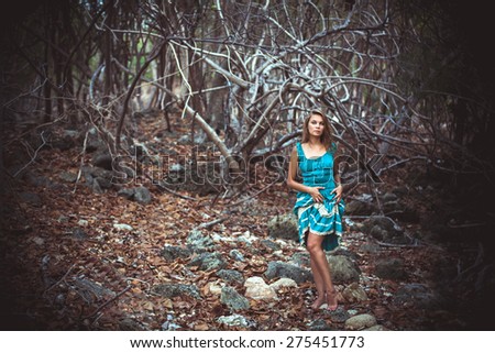 Portrait of a beautiful young woman in turquoise dress standing by trees In jungle forest. Retro colors