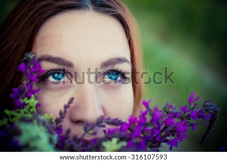 Romantic red-haired young woman smelling a flower on a flower meadow. relaxing on grass