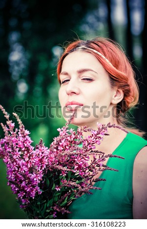 Romantic red-haired young woman in green long dress Walking Through Summer Field Carrying Bouquet Of Flowers