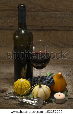 autumnal still life, grapes, pumpkins, candle, cork screw, wine bottle and wine glass on wooden table