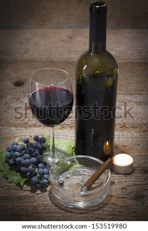 autumnal still life, grapes, candle, wine glass, wine bottle and ashtray with cigar on wooden