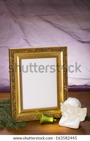 golden frame with pine branch, bell and white plaster angel on wooden in front of purple background