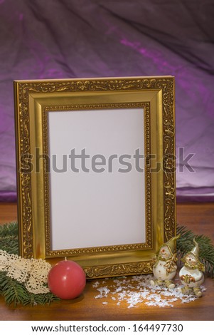 golden frame with christmas candle and figurines on wooden in front of purple background