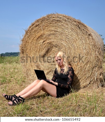 Sexy woman on laptop in hay stack on a summer day