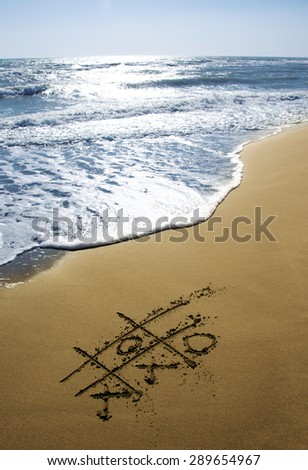 Beach with tic tac toe XO game on sand.