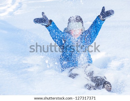 A happy boy is playing with snow on winter